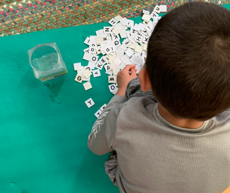 A student sorts letter tiles on the floor