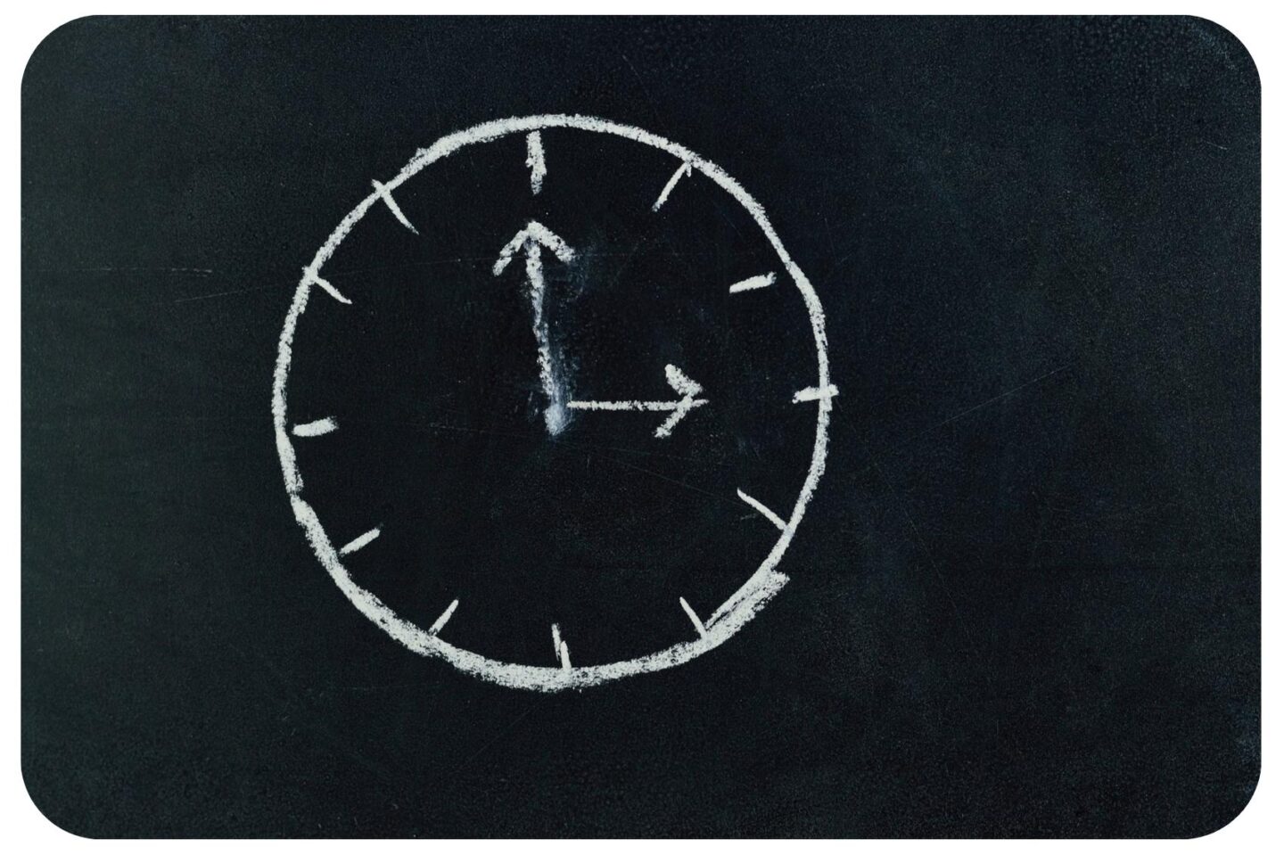 The image features a black chalkboard background. A white chalk analog clock is drawn on it. The hour hand points to the 3 and the minute hand points to the 12. There are no numbers on the clock, only dashes.