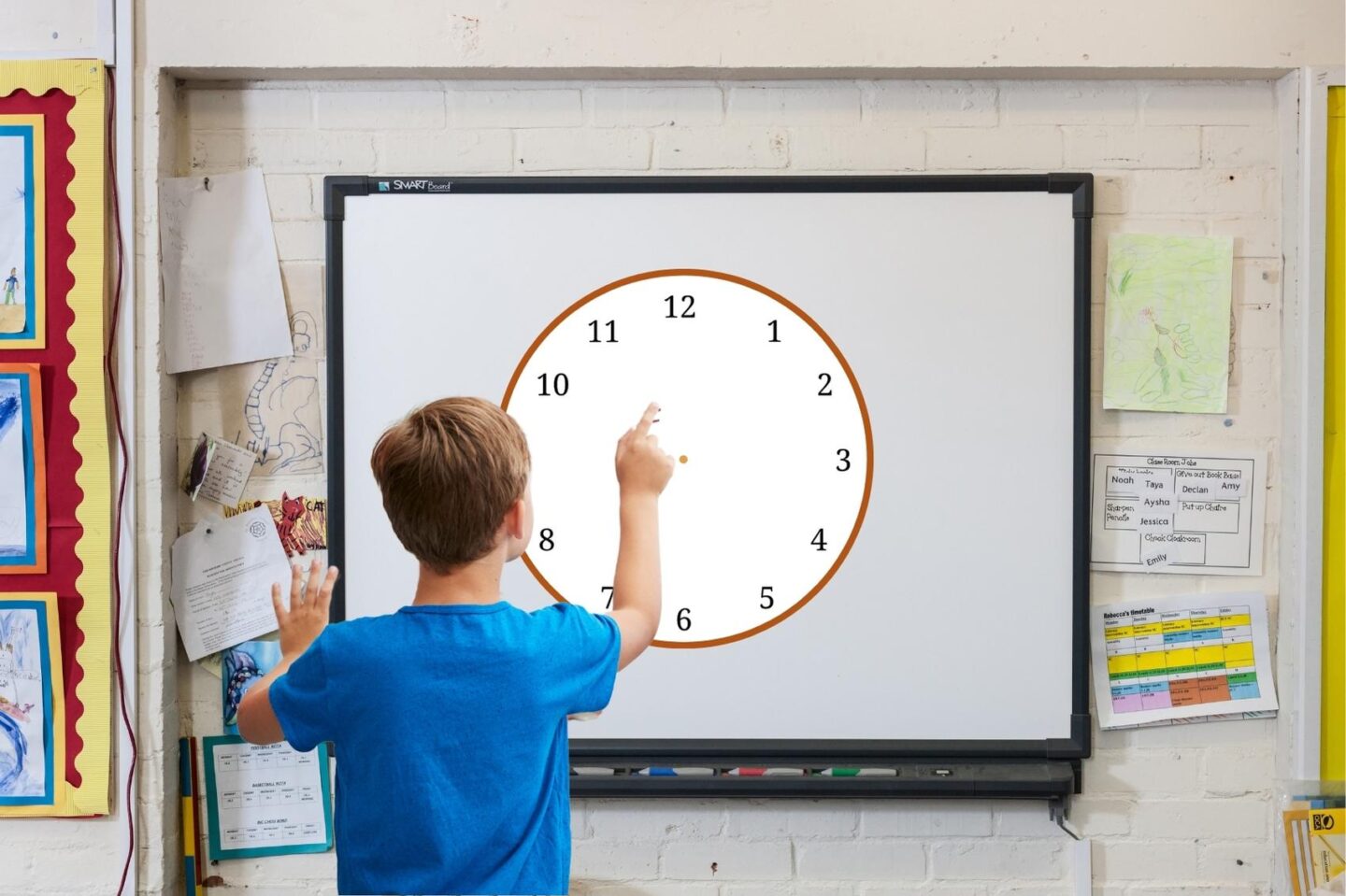 The image shows a whiteboard placed on a classroom wall. The wall is made of white cinder blocks. There are papers taped on the wall to the right and left of the whiteboard. There is a bulletin board to the left of the whiteboard. A boy wearing a blue shirt holds his finger in the air in front of a large clock shown on the whiteboard. There are numbers on the clock but no hands.