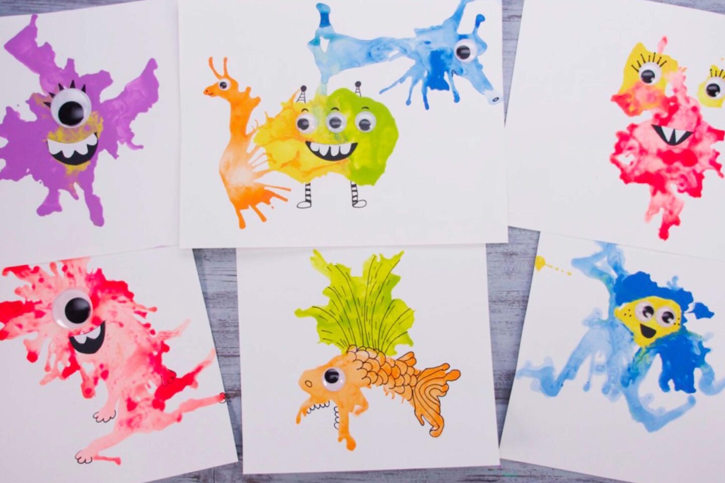 A photo showing one of the Halloween classroom ideas of painting monsters; 6 painted monsters are shown on individual papers with googly eyes and details like arms and scales drawn on with black marker.